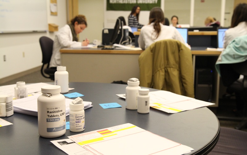 Pharmacy bottles on the table while people are working in the background at the pharmacy practice lab at Northeastern University