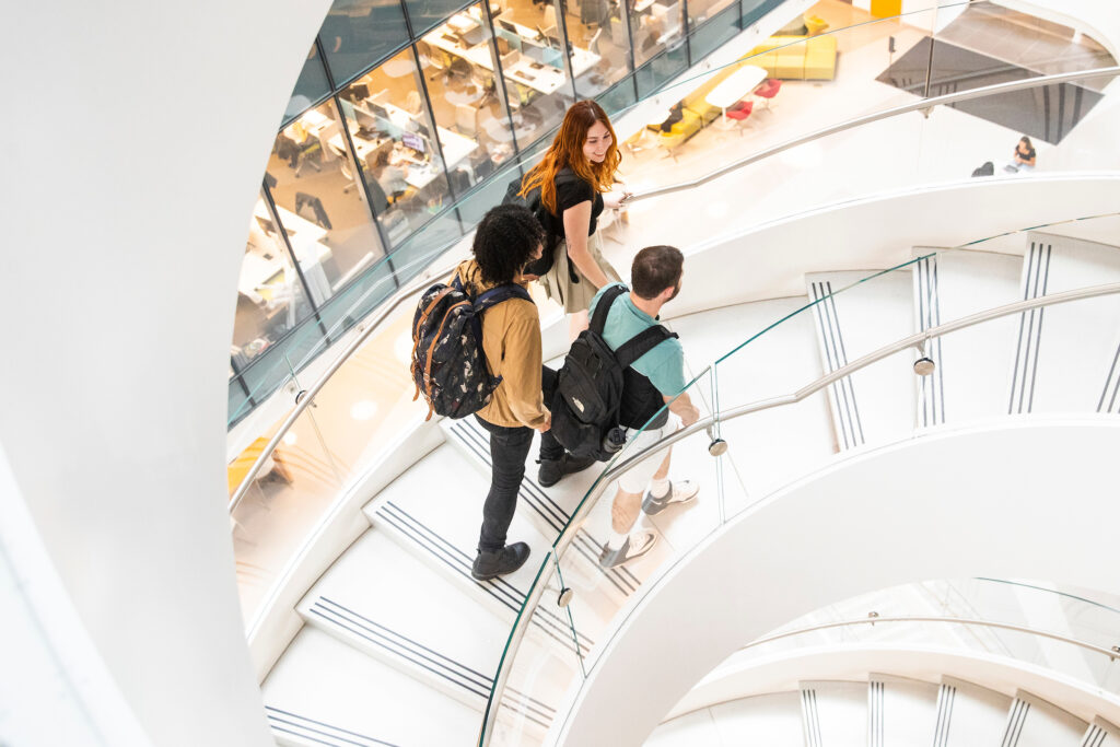 Undergraduate students chatting as they walk up the spiral staircase at the ISEC building at Northeastern University
