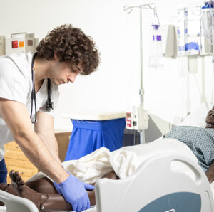 Male nursing student adjusts bed for patient in the SIM Lab