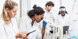 Four people in a lab. One is looking into a microscope.