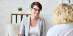 Professional woman in glasses smiles while speaking to another woman.