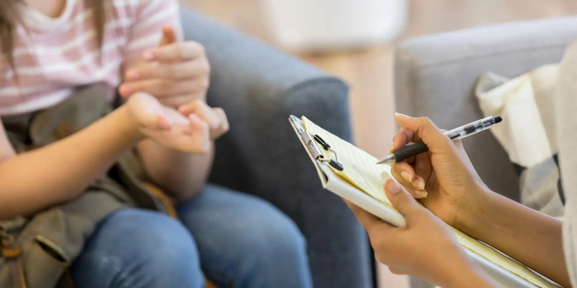 Teenager's hands show emotion while therapist takes notes.
