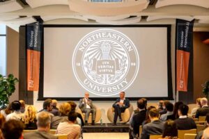 Northeastern President Joseph E. Aoun and David Roux presenting a fireside chat among audience in East Village