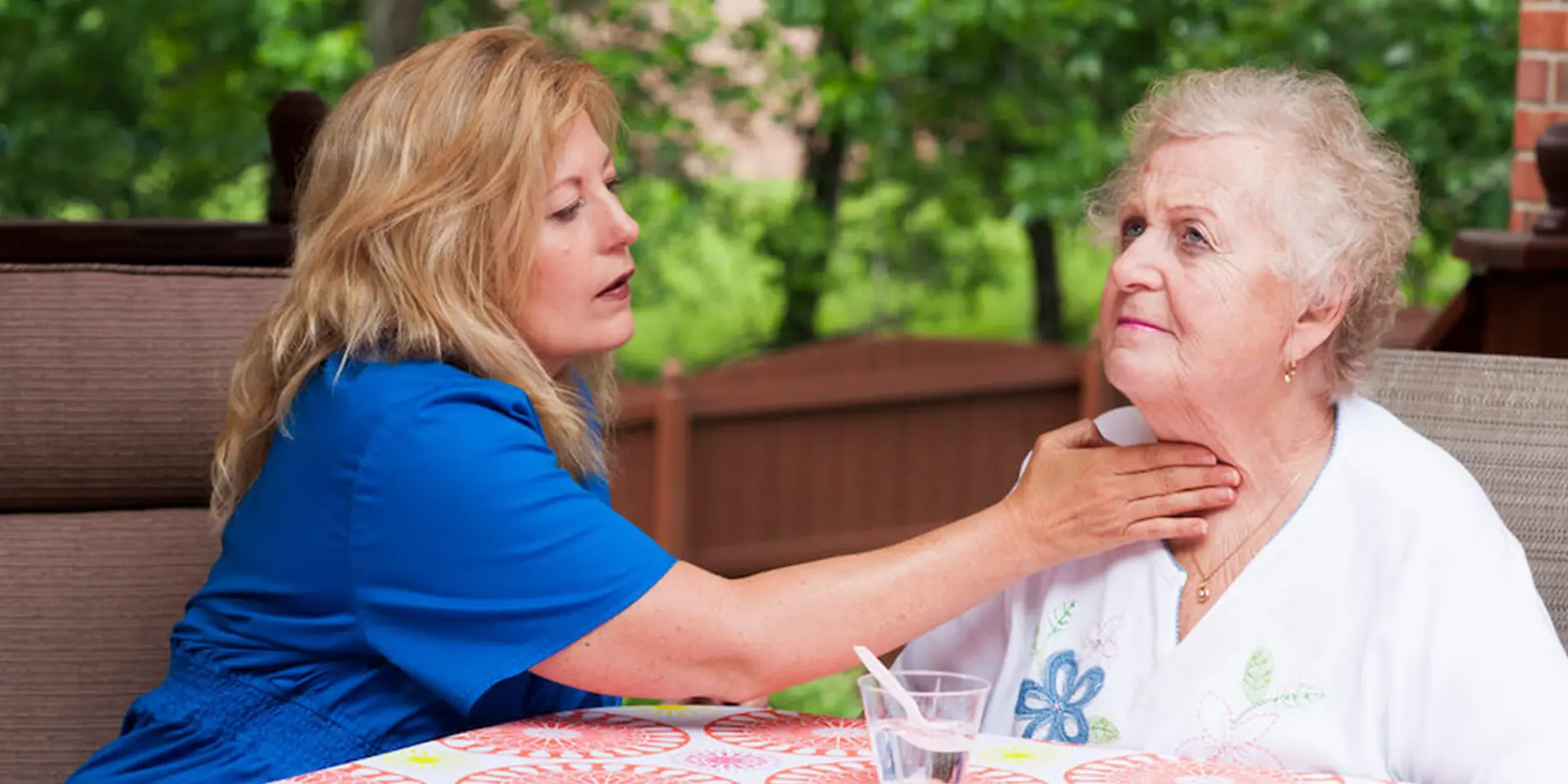 A medical speech-language pathologist has their hand on the throat of an older person. They are outside.