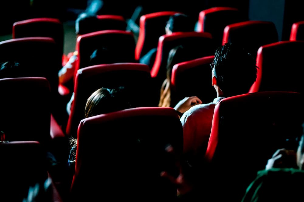 Photo from behind the seats of a movie theater where people are watching the screen