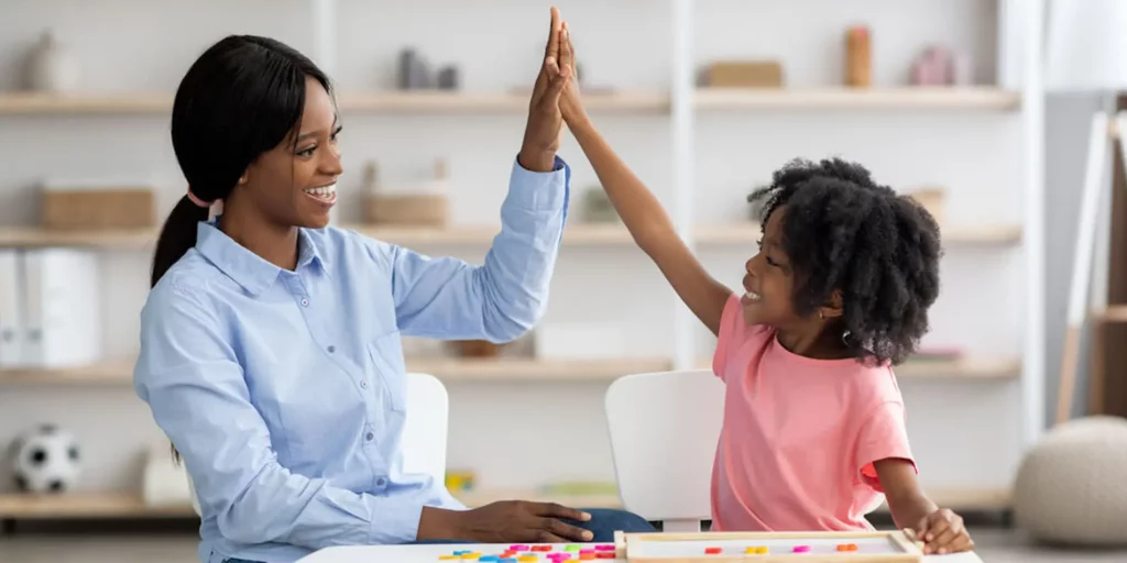 A person high fives a young person. They are looking at each other in a classroom.