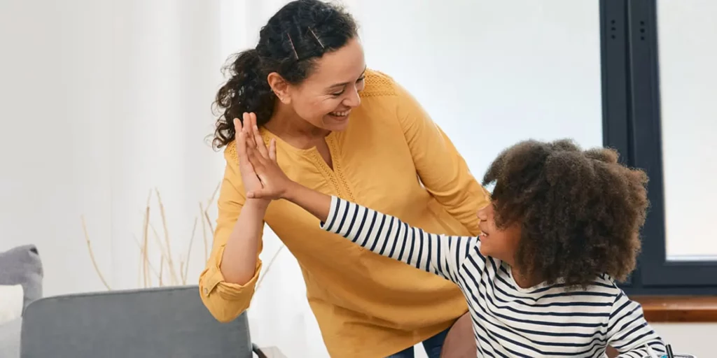 A person is high-fiving a young person. They are in a room with white walls.