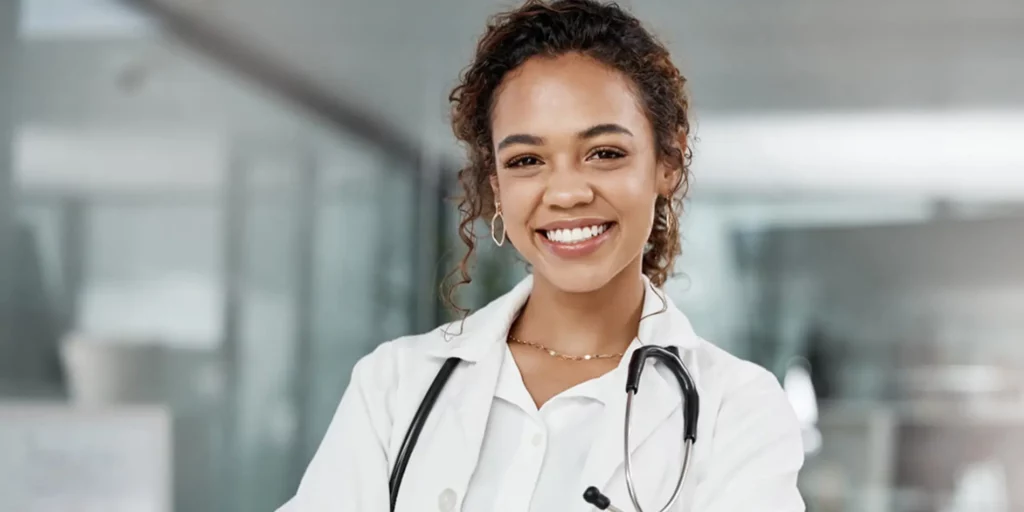 A smiling woman in a white lab coat. A stethoscope is around her neck.