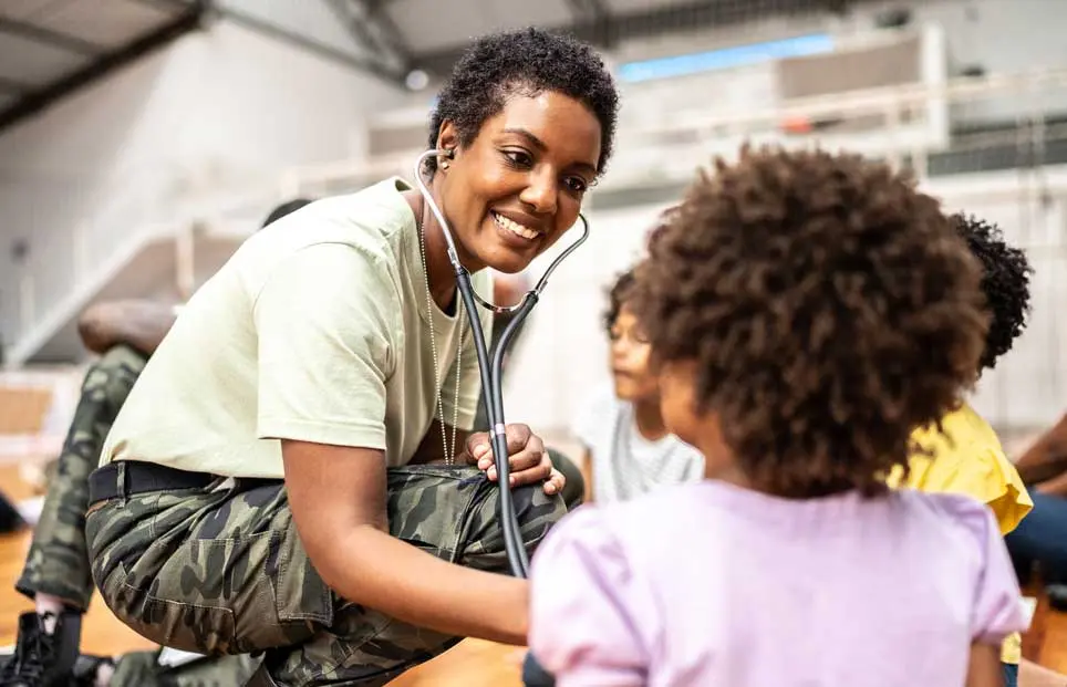 Black army doctor checking little girl's vitals in a camp.