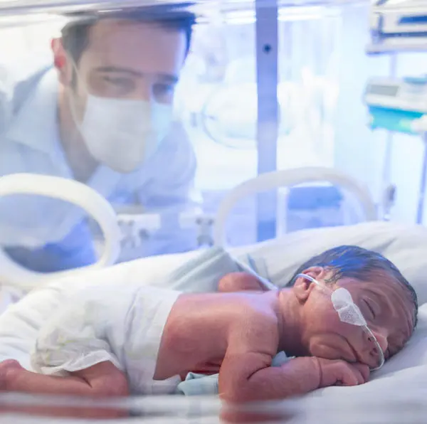 New dad peering through incubator at new born
