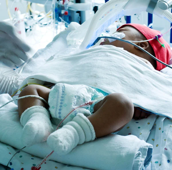 ICU baby of color with little red hat on his head