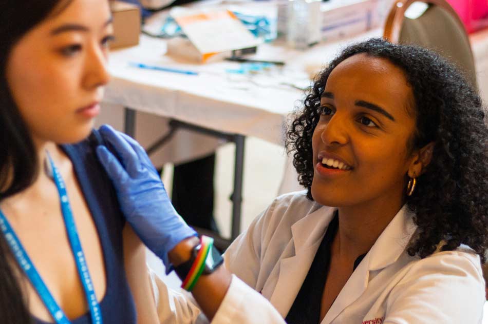 Pharmacy student of color giving flu shots at Northeastern University's student health fair