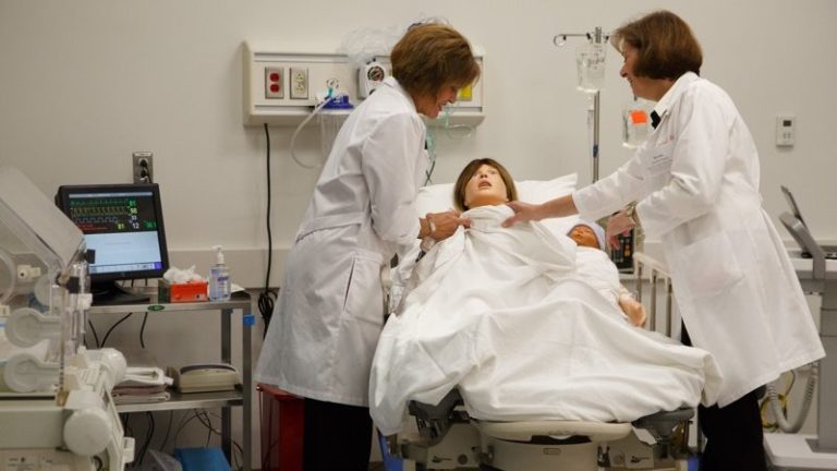 Two students interacting with a robot patient in a simulation of a hospital ward