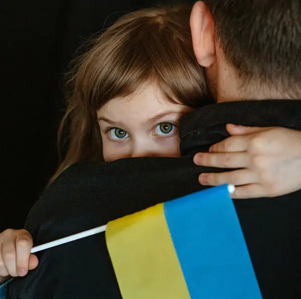 Little Ukrainian girl looking over her father's shoulder and holding a Ukrainian flag