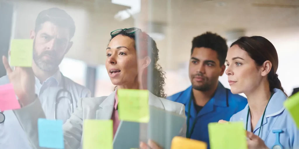 A group of doctors looking at sticky notes on a glass wall.