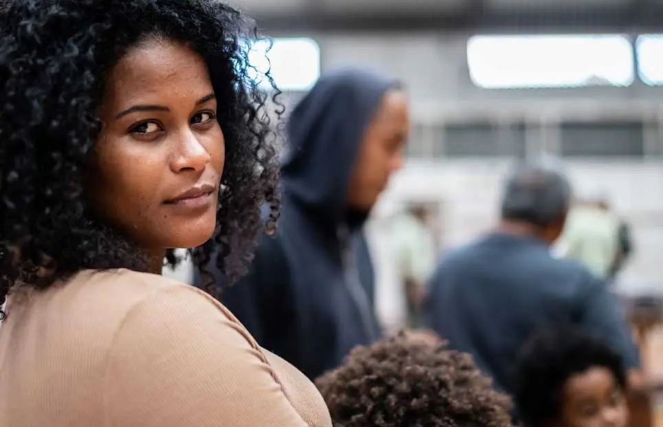 Woman of color refugee in line looking back at camera with challenging look in her eyes