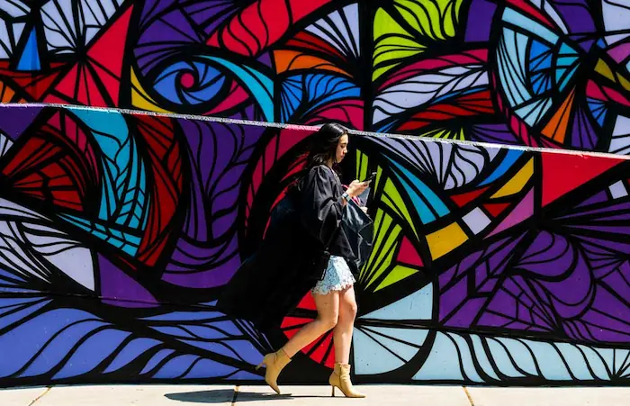 Graduate student walking on campus with a mural in the background.