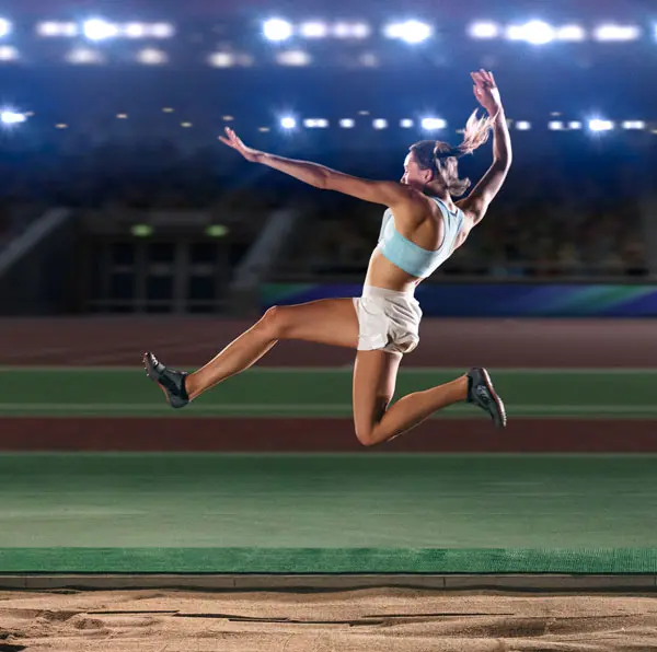 Woman mid long jump competition with arena lights in the background