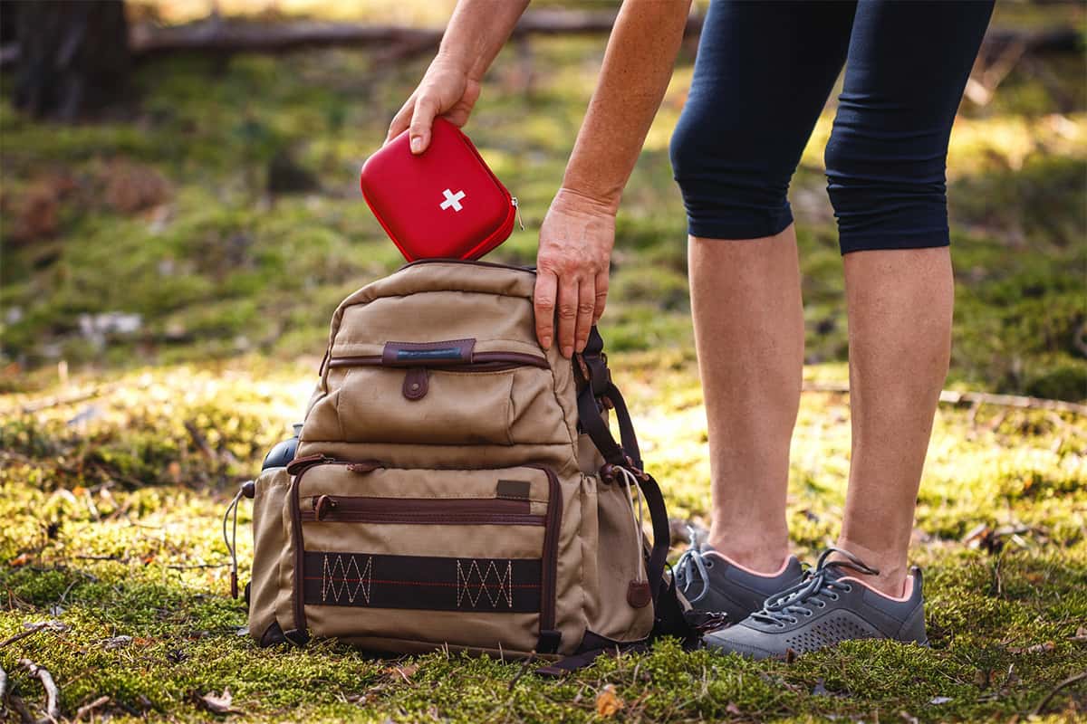 A person outdoors putting a first aid kit into their rucksack