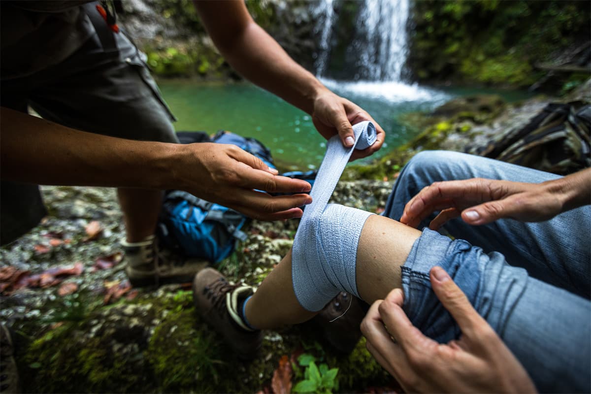 One person bandaging another person's knee in the wilderness