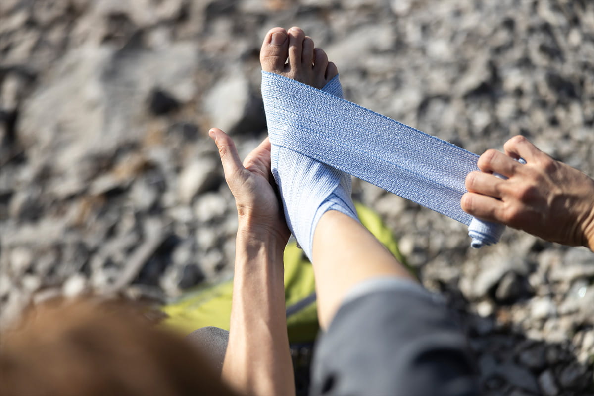 A person wrapping their own foot in a bandage in the wilderness