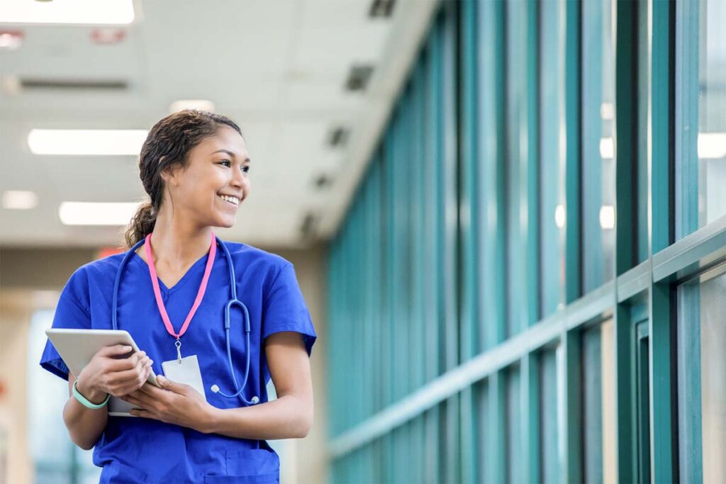 Young female nurse looking out the hospital window smiling.