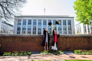Two Northeastern graduates through their caps in the air while posing for photos at Krentzman Quad