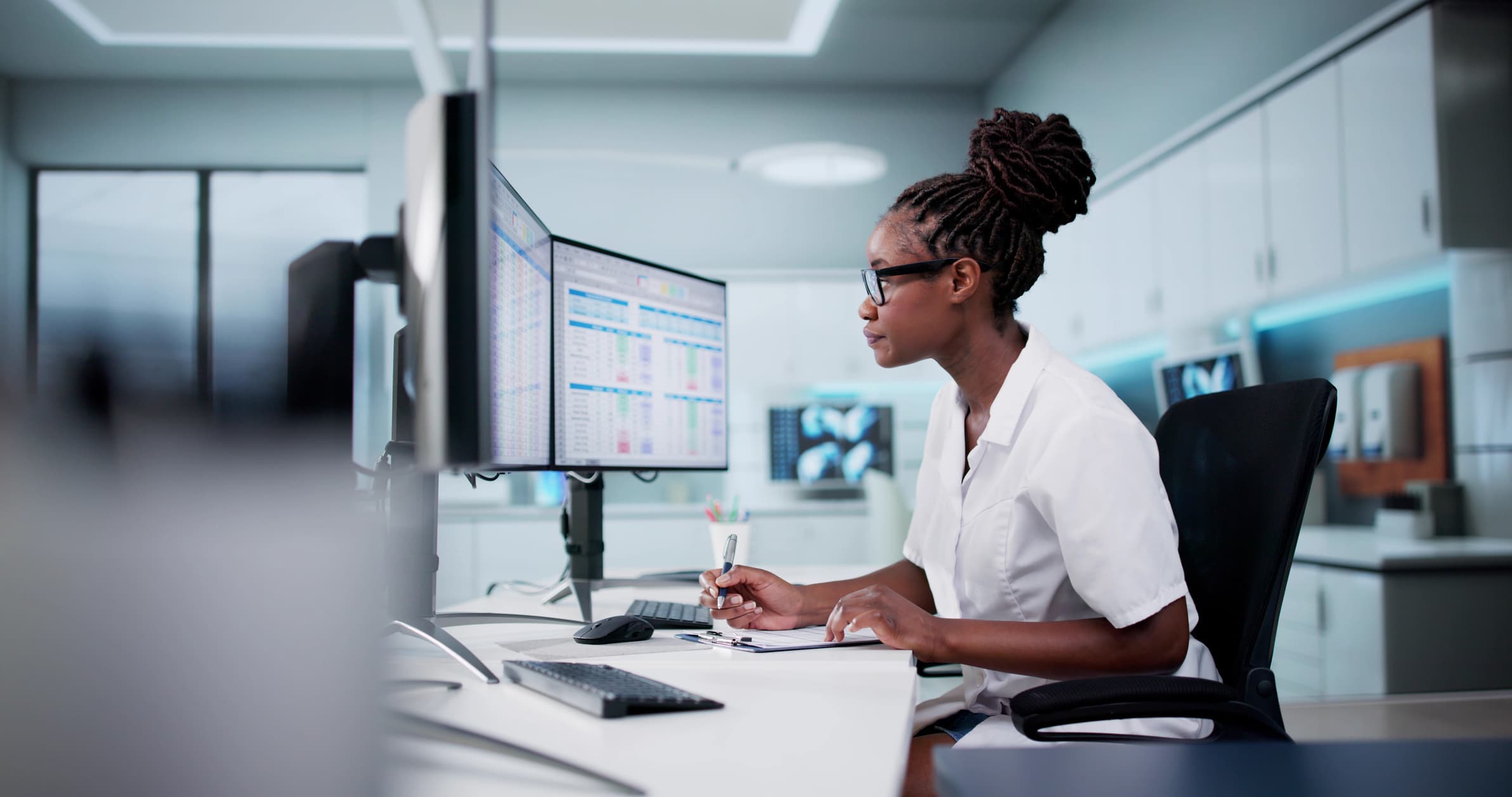 A person taking notes in front of a dual screen monitor.