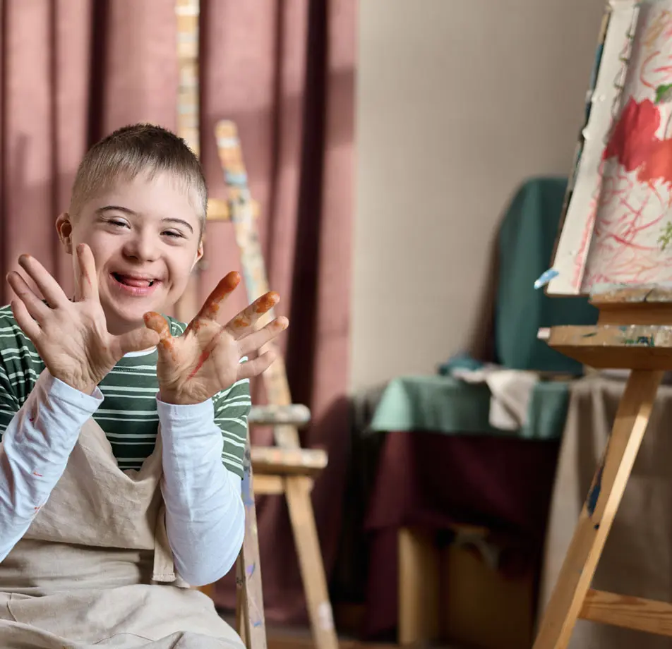 Kid with disabilities smiling and showing his painted hands