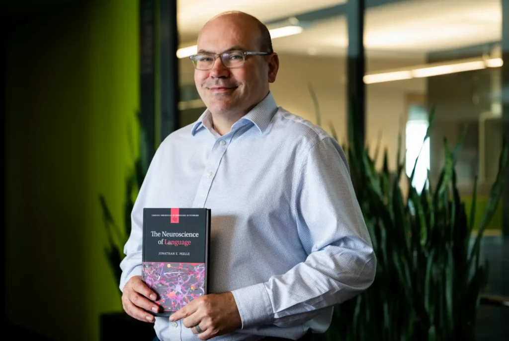 Bouvé's Jonathan Peelle poses holding his new book, “The Neuroscience of Language.”