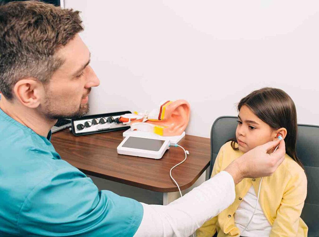 audiologist checks ear of a child, girl having a hearing test