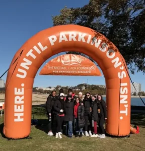 Photo of people at the Michael J. Fox Foundation's Boston Walk/Run standing under an orange, blow-up arch that says "Here. Until Parkinson's Isn't."