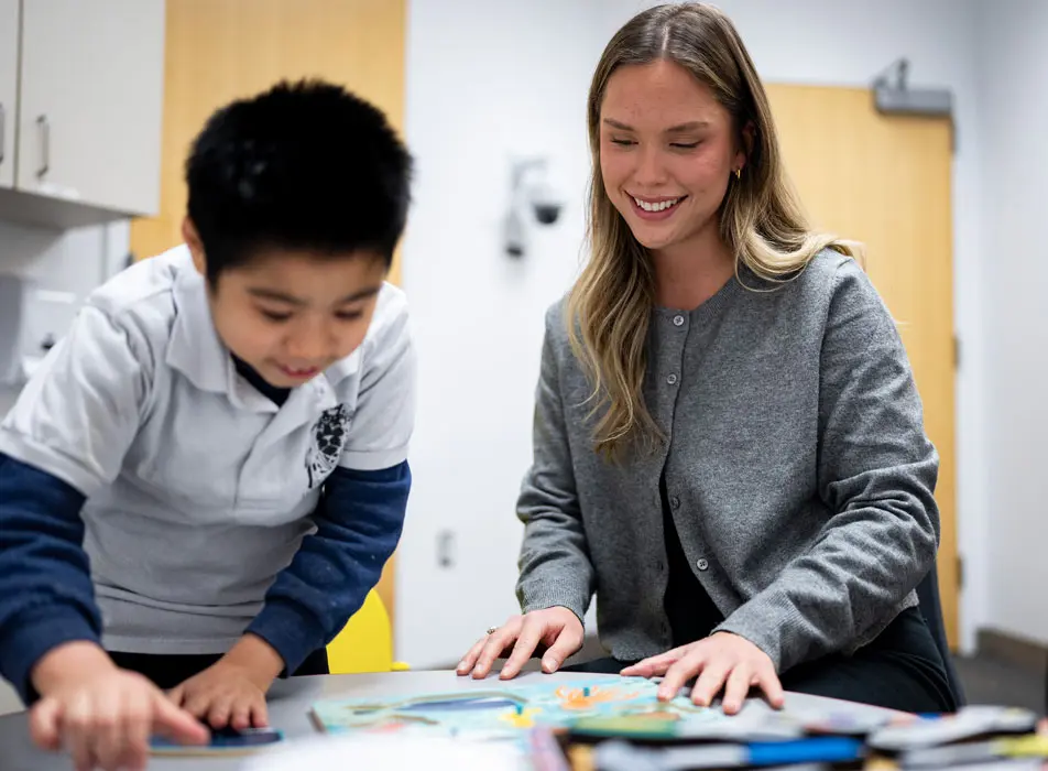 Student assisting child with reading and problem solving at Word Detectives