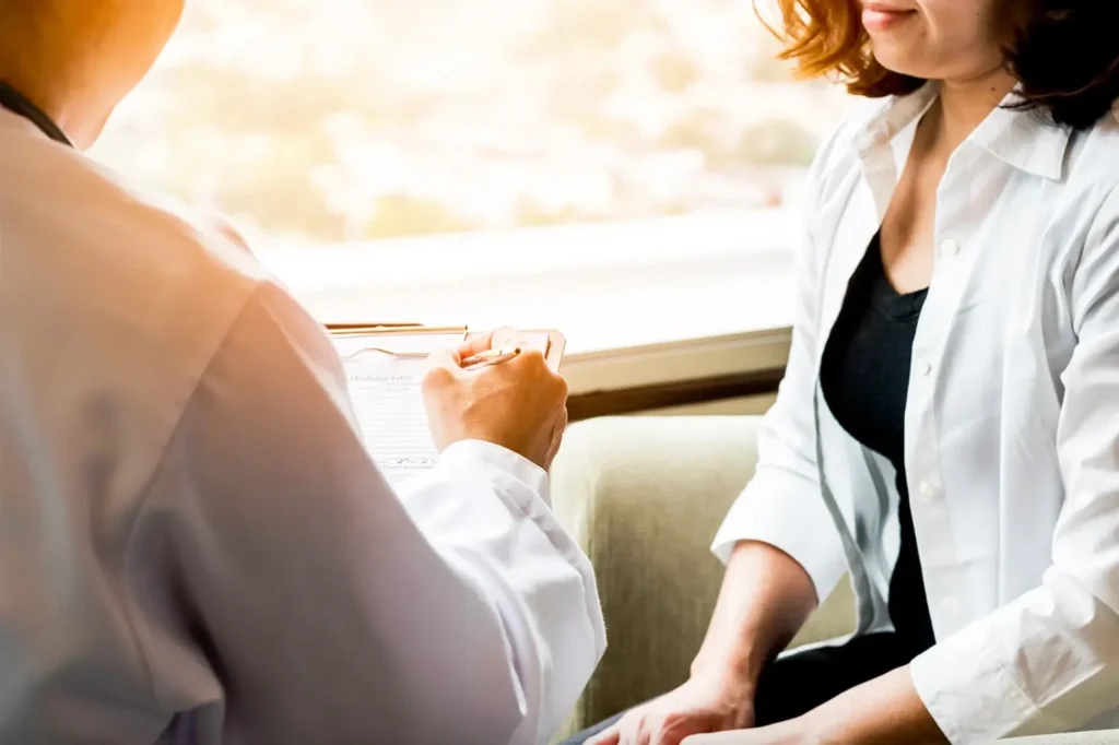 Photo of doctor holding clipboard while talking with female patient
