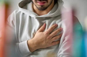 Young man wearing a grey sweatshirt holds his hand over his heart
