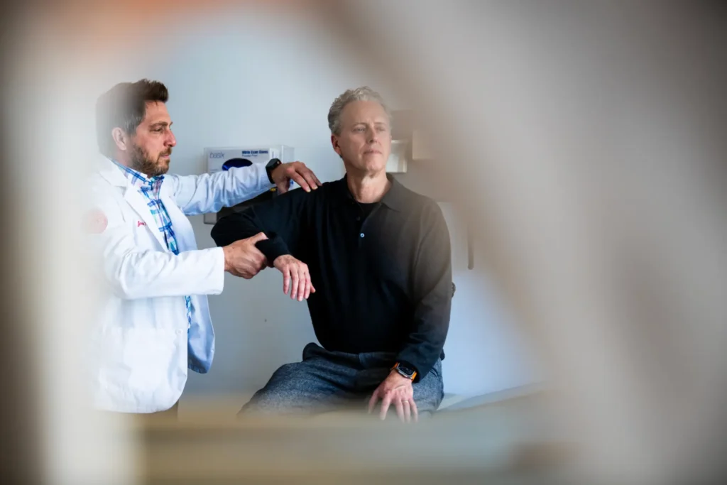 Man in white doctor coat provides a rotator cuff injury evaluation on a man in a doctor's office