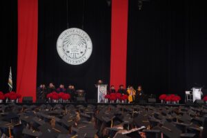 Photo of graduates seated at the Bouvé College Celebration while listening to a speaker at the podium.