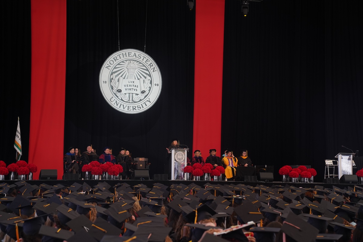 Photo of graduates seated at the Bouvé College Celebration while listening to a speaker at the podium.
